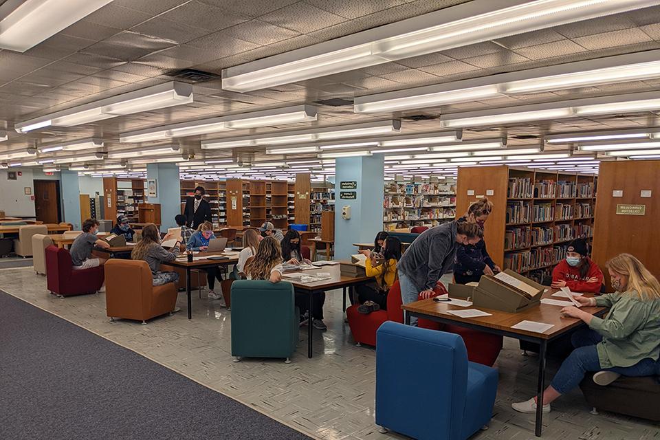 Students examine books while sitting at tables in a library.